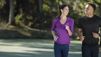 A couple runs together on a park path, smiling and sharing a joyful moment during their outdoor workout
