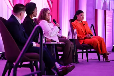Four panelists seated on stage during a conference discussion, with one speaker addressing the audience with a microphone.