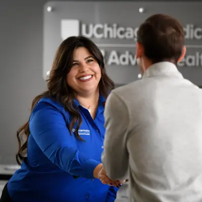 Healthcare professional in blue uniform shaking hands with a person in business attire in front of UChicago Medicine AdventHealth branded signage