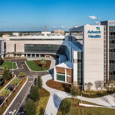 Aerial view of AdventHealth hospital with parking, greenery, and clear blue sky.