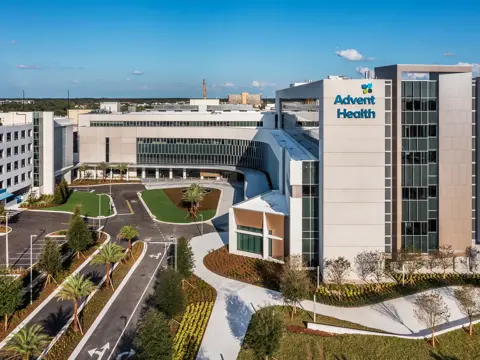 Aerial view of AdventHealth hospital with parking, greenery, and clear blue sky.