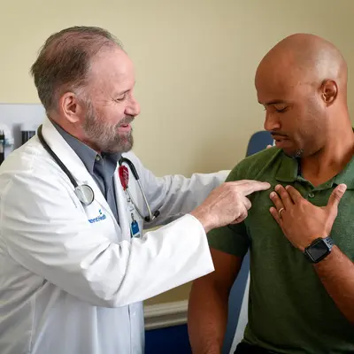 Doctor in white coat examines patient's chest during consultation in exam room