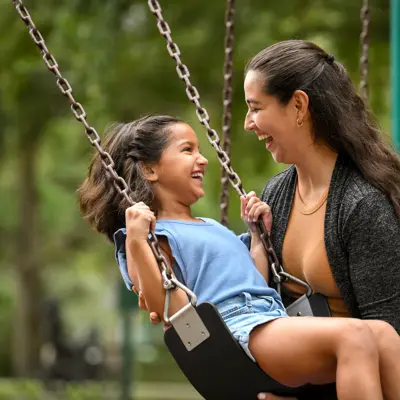 A mother and daughter are laughing and enjoying a swing in a park.