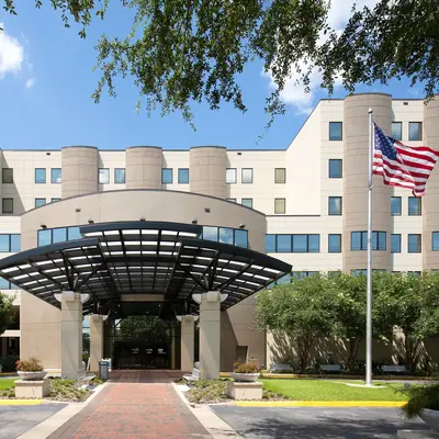 Exterior view of AdventHealth Ocala medical facility featuring a modern curved entrance canopy with an American flag, surrounded by landscaped grounds and trees under a blue sky