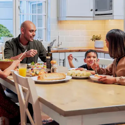 Family of four sharing a meal together at their kitchen table, with a father serving salad to his daughter while the mother and son smile
