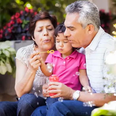 Grandparents and grandchild blowing bubbles together in a garden.