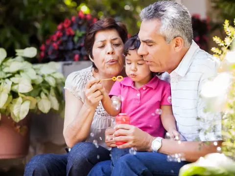 Grandparents and grandchild blowing bubbles together in a garden.
