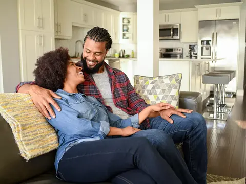 Couple sitting on a couch in a modern kitchen, smiling and holding hands.
