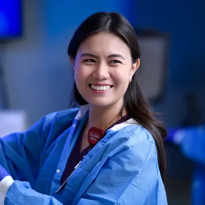 Healthcare professional in blue scrubs and gloves holding a medical syringe in a clinical laboratory setting