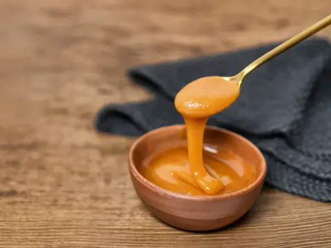 Manuka honey dipper dipping in raw organic liquid from Manuka flowers.