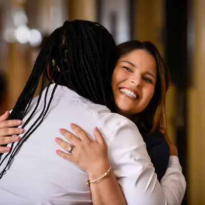 Two nurses in professional attire embracing warmly in a healthcare facility hallway