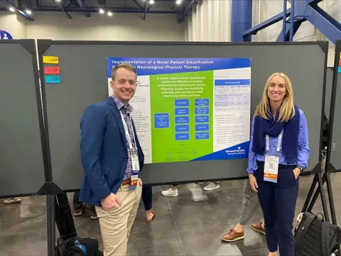 Two people stand beside a poster on patient classification in physical therapy.
