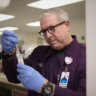 A man in a purple shirt and blue gloves is holding a test tube in a lab.