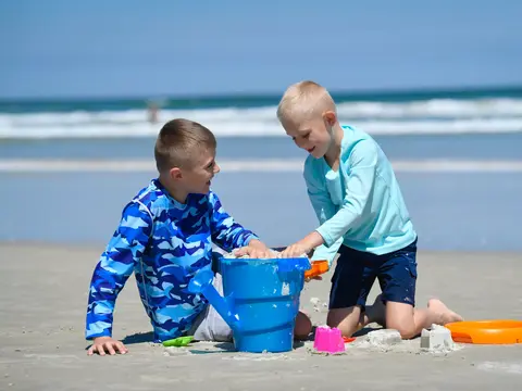 Two boys playing with a blue bucket and sand toys on the beach.