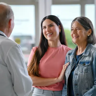 A smiling doctor talks to two smiling women in a hospital setting.