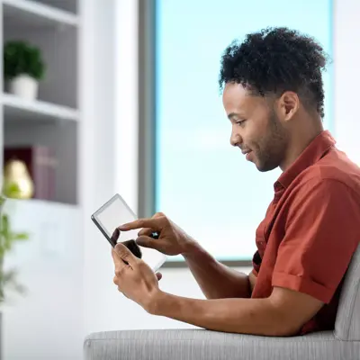 Man sitting on a couch using a tablet, smiling and looking at the screen.