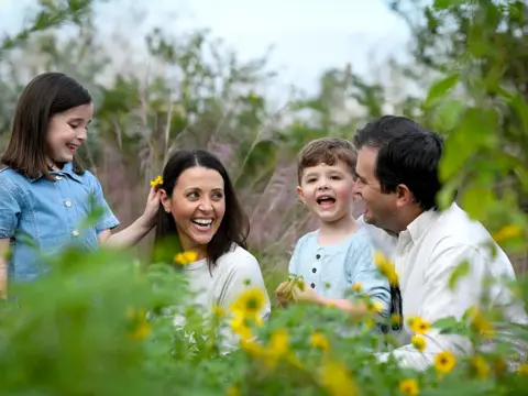 Family of four smiling and laughing in a field of flowers.