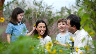 Family of four smiling and laughing in a field of flowers.