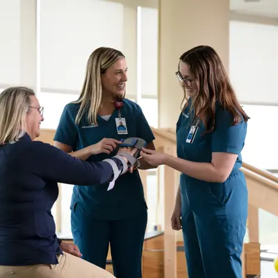 Two nurses assist a patient with a brace on her arm in a rehabilitation setting.
