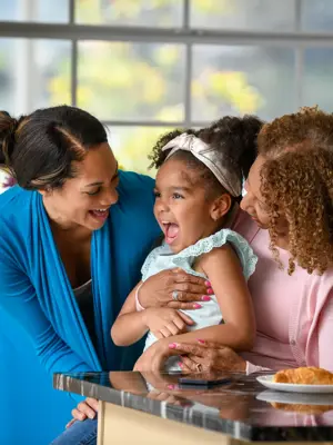 Two women and a young girl share a joyful moment in a bright kitchen, emphasizing family connection and warmth.