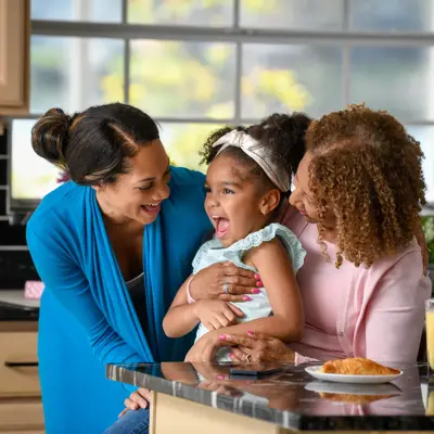 Two women and a young girl share a joyful moment in a bright kitchen, emphasizing family connection and warmth.