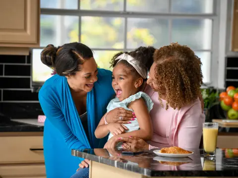 Two women and a young girl share a joyful moment in a bright kitchen, emphasizing family connection and warmth.