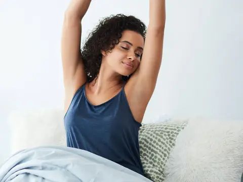 A woman stretches in bed after waking up.