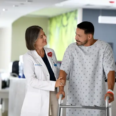 A doctor and a patient using a walker are having a conversation in a hospital hallway.