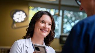 A smiling female doctor in a white coat holds a smartphone, engaging with a patient.