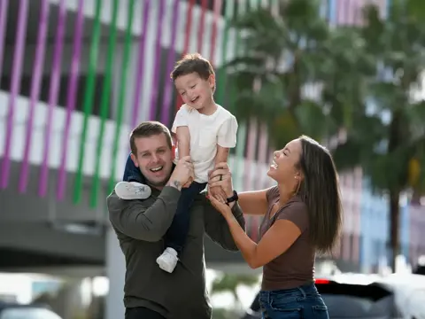 A happy family of three, consisting of a man, a woman, and a child, are smiling and posing for a photo.