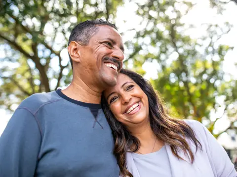 A smiling man and woman stand close together outdoors, embodying warmth and connection.