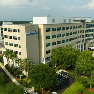 Aerial view of AdventHealth hospital with many windows, surrounded by trees and a parking lot.