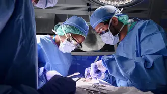 Surgical team of three surgeons in blue scrubs and masks performing a procedure under bright surgical lights in an operating room