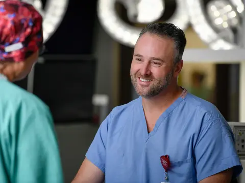 Smiling male surgeon in blue scrubs talks with female colleague in teal scrubs in hospital.