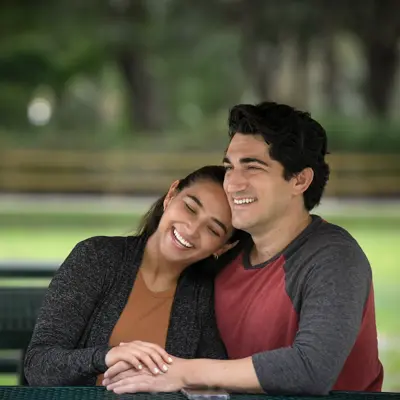 A smiling couple sitting together on a park bench, enjoying each other's company.