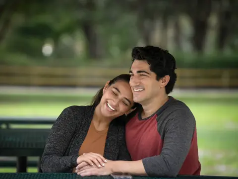 A smiling couple sitting together on a park bench, enjoying each other's company.
