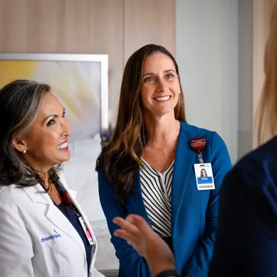 Three AdventHealth employees in a hospital room, smiling and conversing.