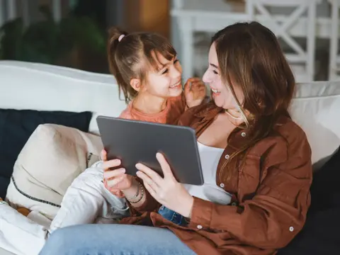 A mom and daughter using a tablet on the couch.