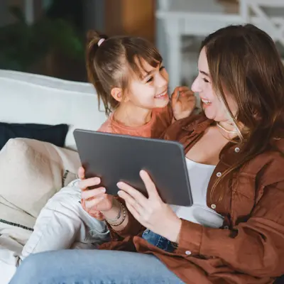 A mom and daughter using a tablet on the couch.
