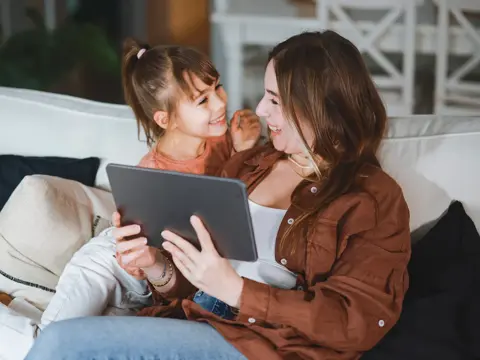 A mom and daughter using a tablet on the couch.