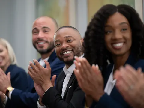 Group of four smiling professionals clapping in an office setting.