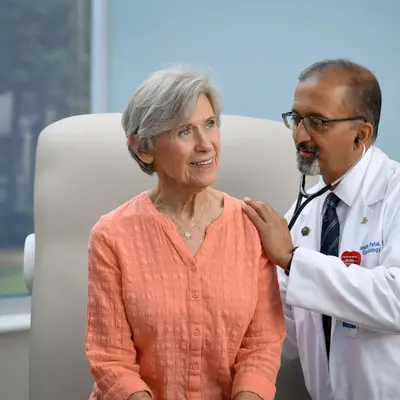 Doctor in white coat with stethoscope examining a female patient wearing a coral blouse in a bright clinical setting