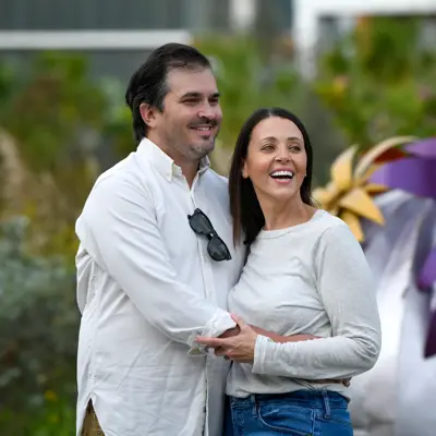 A smiling man and woman stand close together in front of a colorful garden.
