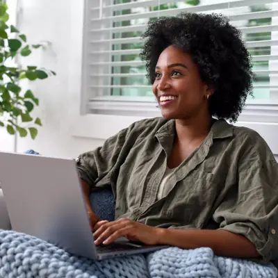 Smiling woman using laptop on couch at home, enjoying a cozy and productive moment.