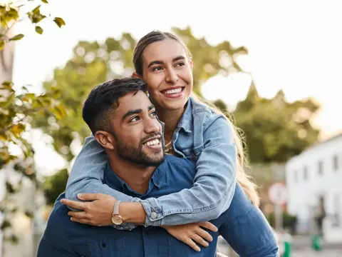 Woman hugging a man from behind while on a walk surrounded by trees
