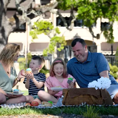Family of four enjoying a picnic on the grass with cupcakes and fruit.