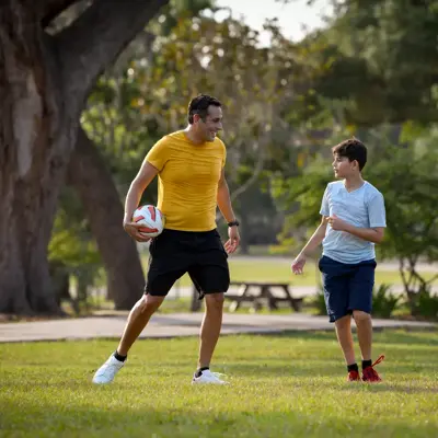 A man and a boy are playing soccer in a park, with the man holding a soccer ball.