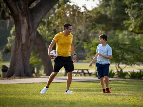 A man and a boy are playing soccer in a park, with the man holding a soccer ball.
