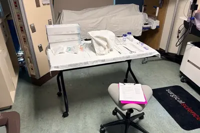 Clinical training room with a table of sterile medical supplies, instruments, and a covered hospital bed prepared for a hands-on procedure.
