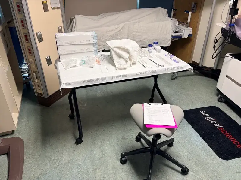 Clinical training room with a table of sterile medical supplies, instruments, and a covered hospital bed prepared for a hands-on procedure.